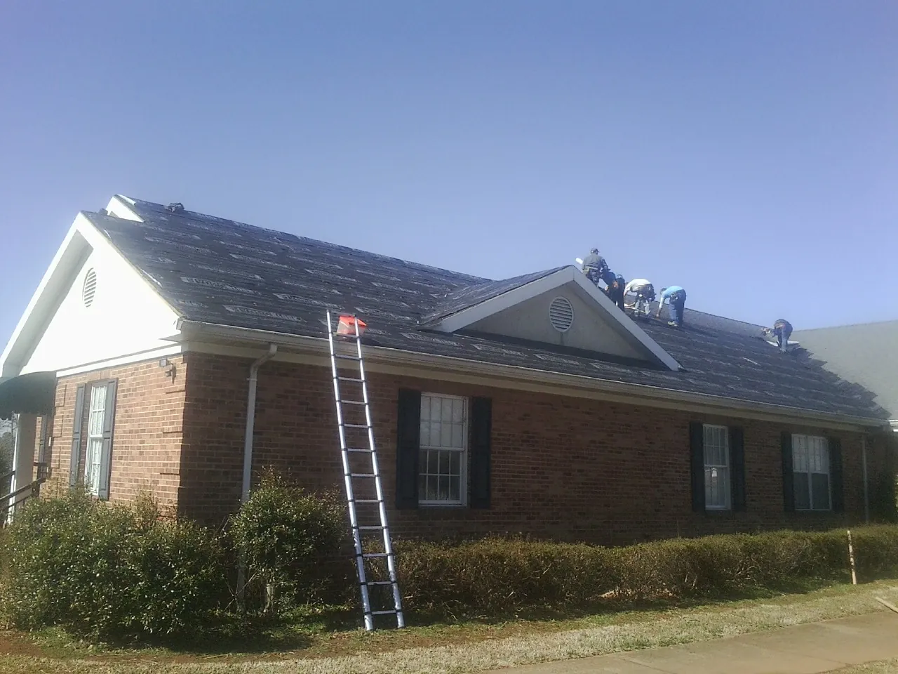 Crew tearing shingles off a brick ranch roof with a ladder set — Metal Roof Repair work by our crew in Elizabethtown