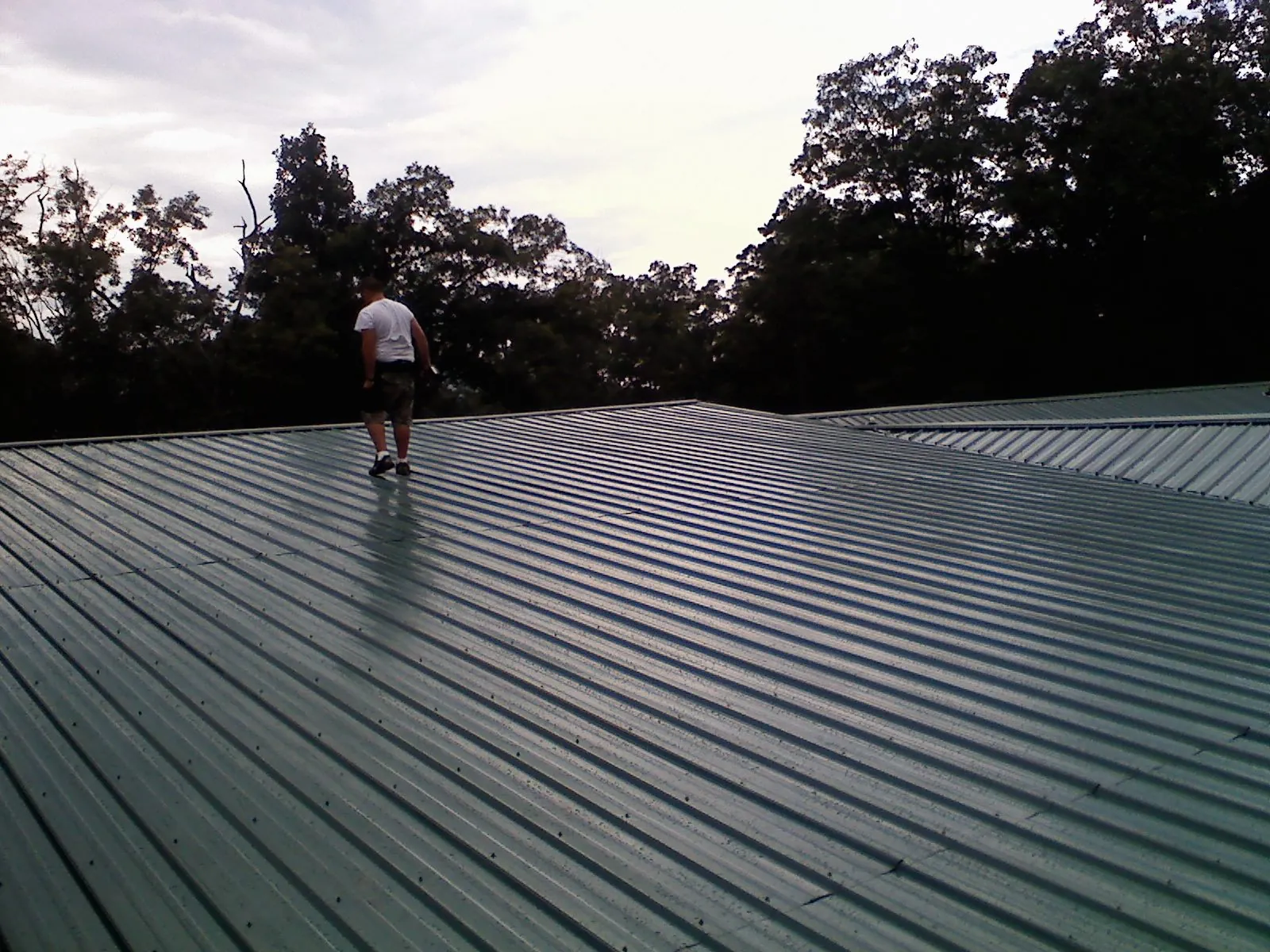 Roofer walking a wide expanse of new green metal roofing in Elizabethtown